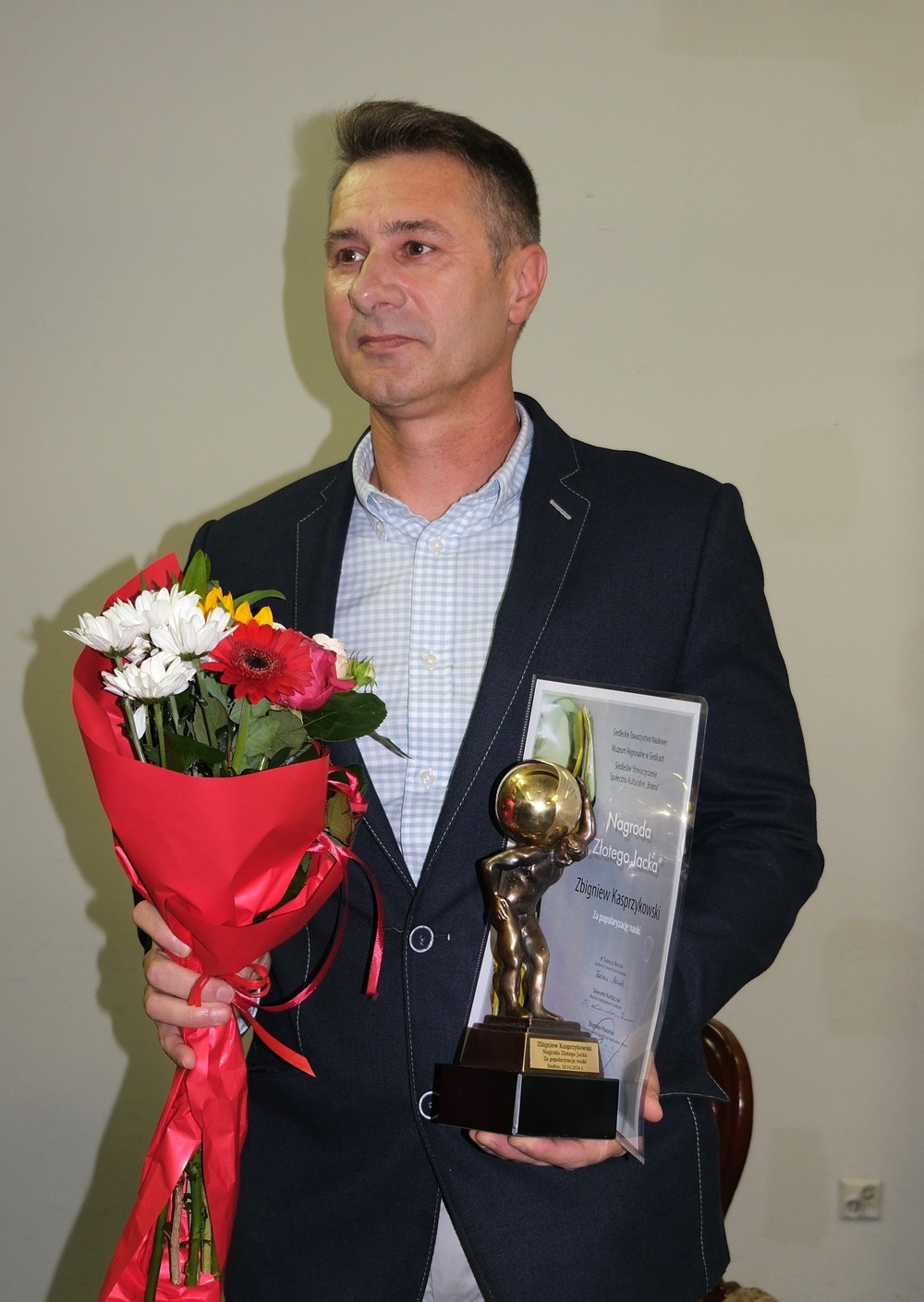 Zbigniew Kasprzykowski trzyma w rękach statuetkę i kwiaty